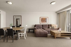 Ein modernes Wohnzimmer mit einem braunen Ecksofa, einem Holztisch und einem Essbereich mit Holztisch und Stühlen.
