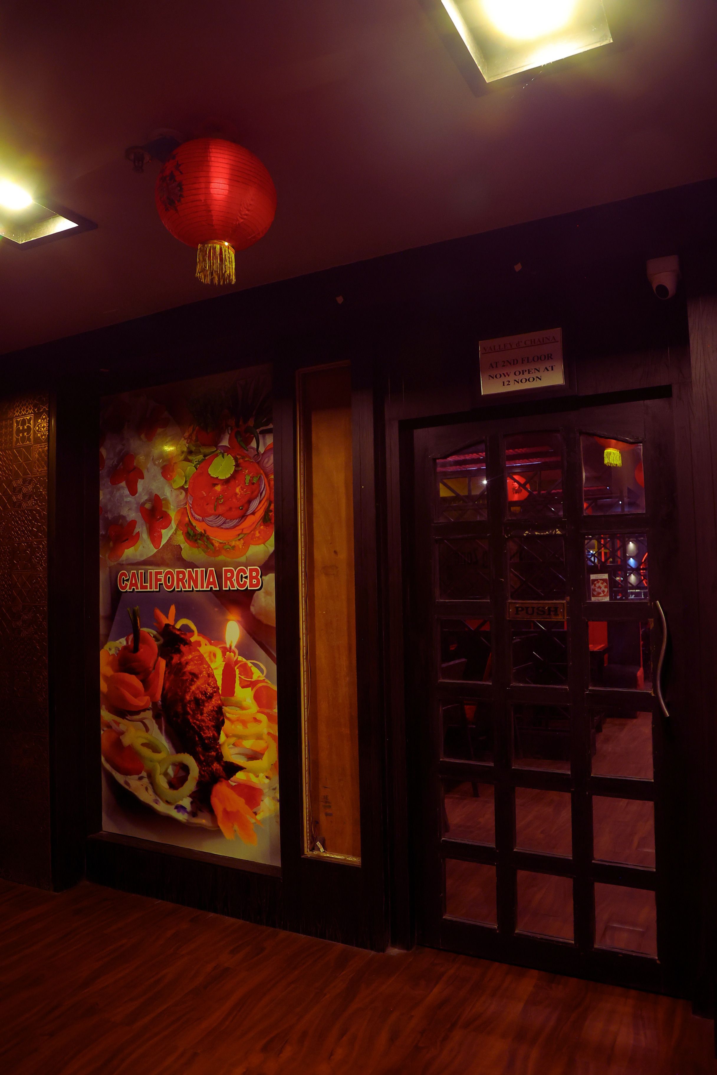 A restaurant interior with a wooden floor, a red lantern, and a sign indicating it's open at 12 noon.