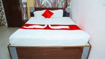 A neatly made bed with a white and red bedspread, a red pillow, and two white towels arranged in a heart shape.