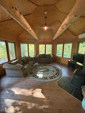 A wooden interior with a sofa, a round rug, and a television. - 4-bedroom log cabin in Gladwin on the Tittawassee River with its own boat launch (Gladwin)