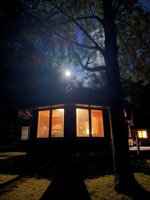 A cabin with a large window, surrounded by trees, and a visible moon in the sky. - 4-bedroom log cabin in Gladwin on the Tittawassee River with its own boat launch (Gladwin)