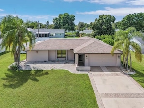 A single-story house with a front garage, a well-maintained lawn, and a clear sky. - Puttputt & pool 3-bedroom house 4 beds, foosball & arcade basketball (Cape Coral)