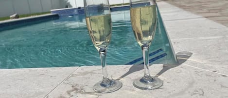Two glasses of a clear liquid on a tiled surface near a swimming pool.