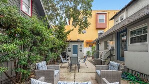A patio area with wicker furniture, a grill, and a yellow building in the background. - StayHaus - The Signature Flat (St. Petersburg)