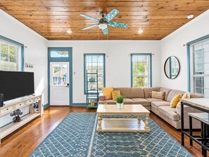 A living room with a wooden ceiling, a ceiling fan, a television, a sofa, a coffee table, and a patterned rug. - Pet-Friendly 2BR Galveston Retreat | Cowboy Pool | Sleeps 8 (Galveston)