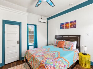 Ein Schlafzimmer mit einem Bett, einem Fenster mit Vorhängen, einem Deckenventilator und Kunstwerken an der Wand.