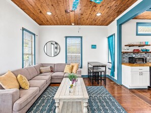 A modern living room with a sectional sofa, a coffee table, and a dining area with a table and chairs. - Pet-Friendly 2BR Galveston Retreat | Cowboy Pool | Sleeps 8 (Galveston)