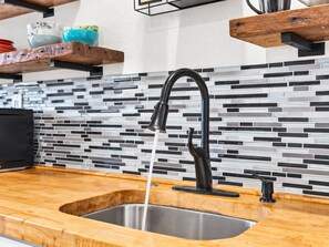 Eine Küche mit einem modernen Wasserhahn, einer Spüle aus Edelstahl und einer Rückwand aus Mosaikfliesen.