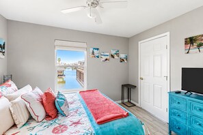 Ein Schlafzimmer mit Bett, Fernseher, Kommode und Blick auf ein Gewässer durch ein Fenster.