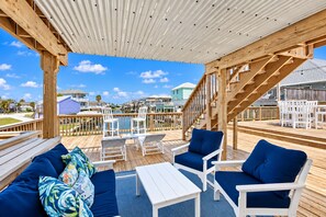 A wooden deck with outdoor furniture, a staircase, and a view of houses in the background. - Galveston Waterfront Home with Private Pool, Dock and Kayaks (Galveston)