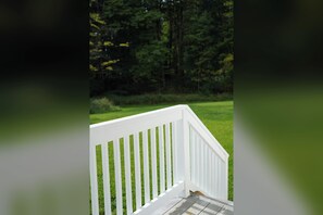A white wooden deck with a view of a grassy area and trees in the background.