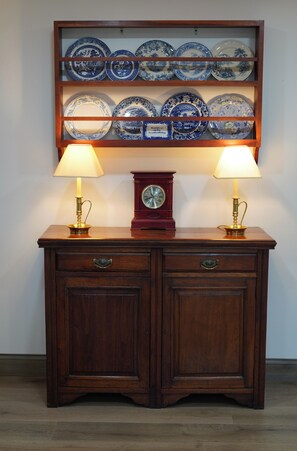 A wooden cabinet with two lamps and a clock, above a shelf with blue and white plates.