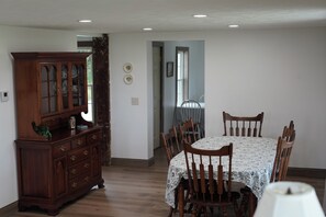 Una sala da pranzo con un tavolo e sedie in legno, un mobile con vetrine e una porta che dà su un'altra stanza.