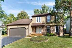 A two-story house with a garage, a front porch, and a well-maintained lawn. - Furnished 4BR • Perfect for Mid-Term Stays (Buffalo Grove)