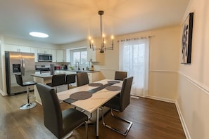 A modern kitchen with a central island, dining area with a table and chairs, and a chandelier.