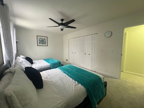 A bedroom with two beds, a ceiling fan, a clock, and a wardrobe.