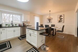 A modern kitchen with white cabinetry, a black countertop, and a dining area with a white table and black chairs. - Furnished 4BR • Perfect for Mid-Term Stays (Buffalo Grove)