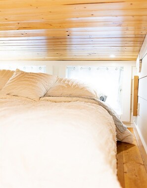 Ein Schlafzimmer mit Holzboden, einem Bett mit weißer Bettwäsche und einem Fenster mit Vorhängen.