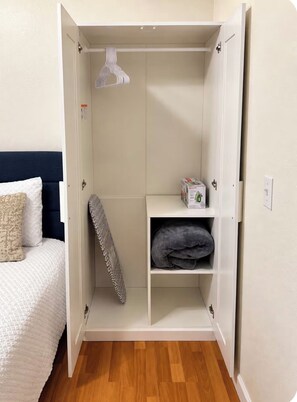 Une pièce comprenant un lit, une armoire et une étagère avec des couvertures pliées.