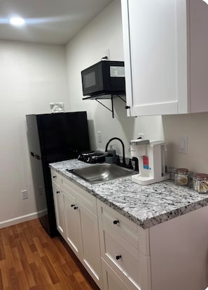 A compact kitchen with white cabinets, a black refrigerator, a microwave, a coffee maker, and a sink. - Cozy 1 bedroom studio in lovely Brandon with AC (Brandon)