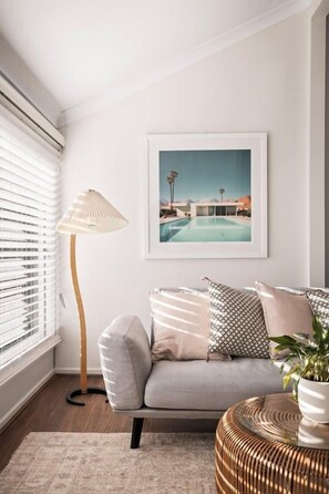 A room with a grey sofa, a framed picture of a pool, a floor lamp, and a woven side table. - Lõco Píso House Pet friendly - Pool & Spa (Brisbane)