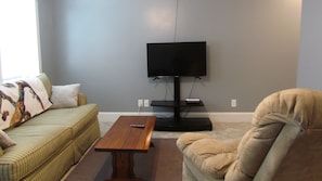 A living room with a sofa, a chair, a coffee table, and a television against a wall. - Downstairs carriage house on Columbus (Savannah)