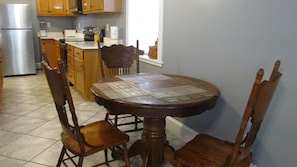 A kitchen with wooden cabinets, a stainless steel refrigerator, a dining table with a placemat, and two wooden chairs. - Downstairs carriage house on Columbus (Savannah)