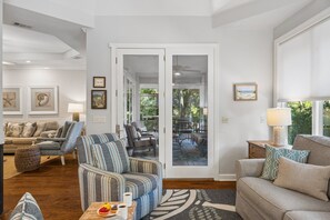 Ein geräumiges Wohnzimmer mit einer Couch, Sesseln und einem Couchtisch. Es gibt einen Essbereich mit Stühlen und einem Tisch. Das Zimmer hat ein großes Fenster und eine Tür, die zu einer Außenpatio führt.