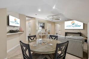 Ein modernes Wohnzimmer mit Essbereich, Deckenventilator und Fernseher mit dem 'HOST & Home'-Logo.