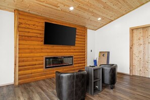 Une pièce avec un mur en bois, un téléviseur à écran plat, une cheminée et des fauteuils en cuir.