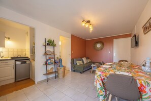 A compact living space with a kitchenette, a dining area with a table and chairs, and a sofa. - The Marine Apartment with Terrace & Garden - Welkeys (Villers-sur-Mer)