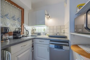 A compact kitchen with white cabinets, a coffee maker, a kettle, and a dishwasher. - The Marine Apartment with Terrace & Garden - Welkeys (Villers-sur-Mer)