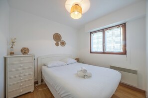 A bedroom with a bed, a dresser, a wall-mounted lamp, and a window with curtains. - The Marine Apartment with Terrace & Garden - Welkeys (Villers-sur-Mer)