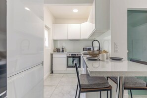 A modern kitchen with white cabinetry, a stainless steel oven, and a dining area with a marble countertop and two chairs. - La Perle du Mourillon 5 minutes from the beach - Welkeys (Toulon)