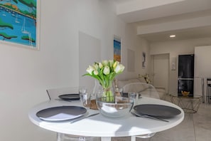 Een eetgedeelte met een ronde tafel, witte borden en een vaas witte bloemen.