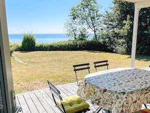 Eine Terrasse mit Tisch und Stühlen, mit Blick auf eine Rasenfläche und ein Gewässer.