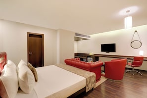 A hotel room with a bed, a red sofa, a desk, a chair, and a television. - The Phlox Hotel (Hubli)