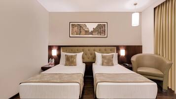 Ein Hotelzimmer mit zwei Betten, einem Kopfteil, Nachttischen, einer Lampe, einem Sessel und einem gerahmten Bild an der Wand.