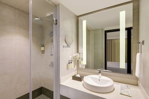 A modern bathroom with a glass shower enclosure, a sink with a mirror, and toiletries on the countertop. - The Phlox Hotel (Hubballi)