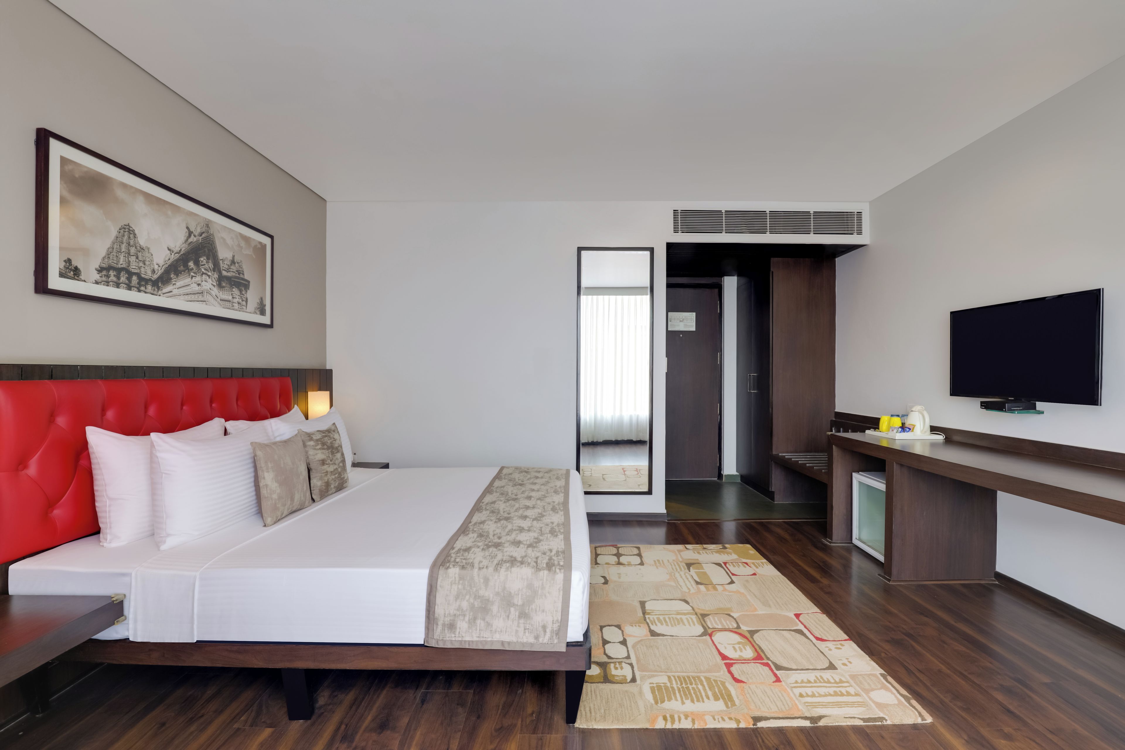 Habitación de hotel con una cama grande, un televisor de pantalla plana, un escritorio y un baño visible a través de una puerta abierta.