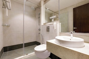 A modern bathroom with a glass-enclosed shower, a white toilet, and a sink with a mirror above it. - The Phlox Hotel (Hubli)