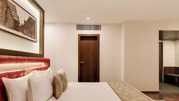 Quarto de hotel com uma cama grande, cabeceira estofada em vermelho, um quadro na parede e uma porta que dá para outro cômodo.