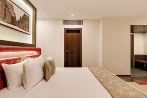 A hotel room with a large bed, a red upholstered headboard, a framed picture on the wall, and a door leading to another room.