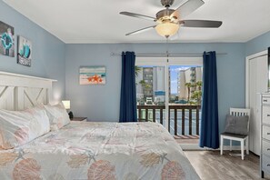 A bedroom with a bed, a ceiling fan, a view of the outside, and a window with curtains. - Summer Place 127 | Sleeps 6 | Great Fall Break Vacation! (Panama City)