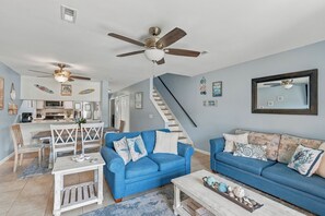 A living room with two blue sofas, a coffee table, and a dining area with a white table and chairs. - Summer Place 127 | Sleeps 6 | Great Fall Break Vacation! (Panama City)