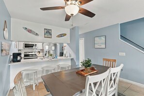 A kitchen with white cabinets, a microwave, and a refrigerator. There is a dining table with chairs and a ceiling fan above. - Summer Place 127 | Sleeps 6 | Great Fall Break Vacation! (Panama City)