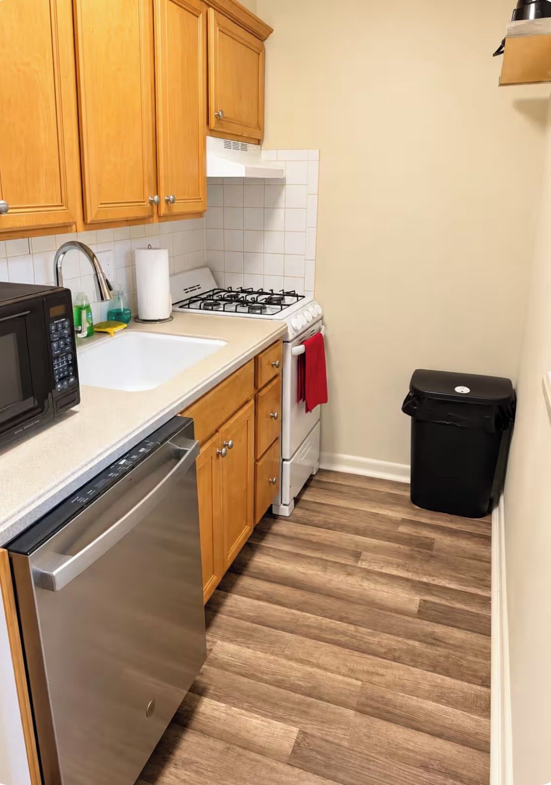 Una cucina con mobili in legno, una lavastoviglie in acciaio inox, un piano cottura a gas e un cestino per i rifiuti.