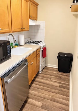 Una cucina con mobili in legno, una lavastoviglie in acciaio inox, un piano cottura a gas e un cestino per i rifiuti.