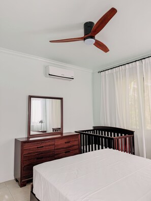 A bedroom with a bed, a crib, a dresser, a mirror, an air conditioning unit, and a ceiling fan. - The Snapdragon Courtyard Garden (Montego Bay)