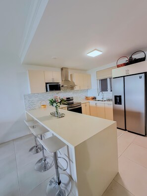 A modern kitchen with a central island, stainless steel appliances, and a white color scheme. - The Snapdragon Courtyard Garden (Montego Bay)